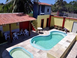 Piscina com área de cobertura vermelha e cadeiras brancas.