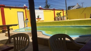Ein Swimmingpool mit gelber Wand und Tür, umgeben von Stühlen und einem Tisch.