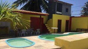 A swimming pool area with two pools, a small table, and a staircase leading to a building. - Top Home Pousada (Caucaia)