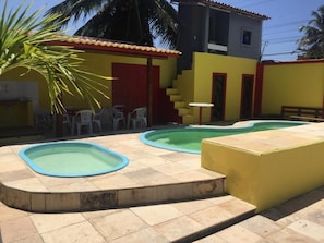 Ein Poolbereich mit zwei Schwimmbecken, einem kleinen Tisch und einer Treppe, die zu einem Gebäude führt.