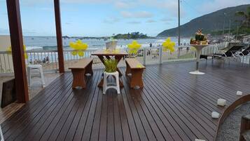 Terraza de madera con mesa y sillas, con vista a una playa y al océano.