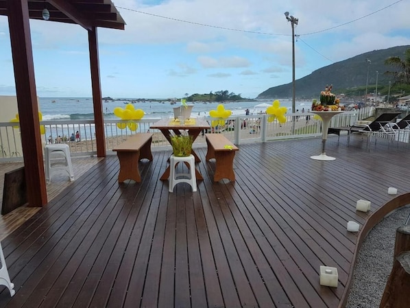 A wooden deck with a table and chairs, overlooking a beach and ocean. - Frente Mar (Florianópolis)