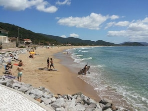 A beach with people, a rocky shoreline, and a clear sky. - Frente Mar (Florianópolis)