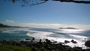 Un paisaje costero con un primer plano rocoso, una playa y un cielo despejado.