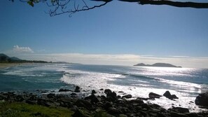 A coastal landscape with a rocky foreground, a beach, and a clear sky. - Frente Mar (Florianópolis)