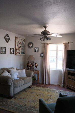 Ein Wohnzimmer mit einer Couch, einem Fernseher, einem Deckenventilator und Wanddekoration.
