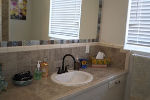 A bathroom with a white sink, black faucet, and a mirror above it. There are toiletries on the counter and a towel rack to the right. - Historic charming 2-bedroom house with AC in welcoming Tucson (Tucson)