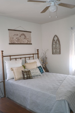 A bedroom with a bed, a ceiling fan, a wall-mounted picture, and a window with a curtain. - Historic charming 2-bedroom house with AC in welcoming Tucson (Tucson)