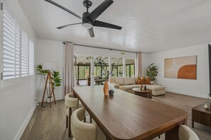 A modern living room with a wooden dining table, beige sofa, and a ceiling fan. - LongBeach Cottage - Pool, Spa, Games, 4Miles2Beach (Long Beach)