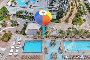 A hotel with multiple swimming pools, a large colorful water balloon sculpture, and palm trees. - Beautiful Apt w/Balcony & Beachfront Resort + Pool (Hollywood)