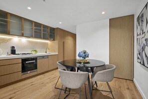 A modern kitchen with wooden cabinets, a built-in oven, and a dining area with a round table and four chairs. - High-Rise 1-Bed Apartment in Melbourne CBD (Melbourne)
