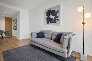 A modern living room with a grey sofa, a dark grey rug, and a floor lamp with three lights. - High-Rise 1-Bed Apartment in Melbourne CBD (Melbourne)