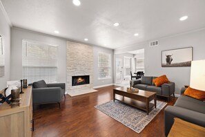 A modern living room with a fireplace, hardwood flooring, and contemporary furniture. - Hot Spa Private Oasis Also Available for long term (McKinney)