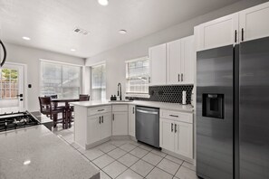 A modern kitchen with white cabinetry, a stainless steel refrigerator, and a dishwasher. - Hot Spa Private Oasis Also Available for long term (McKinney)