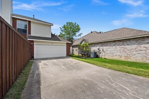 A residential driveway leading to a garage, a brick house, and a wooden fence. - Hot Spa Private Oasis Also Available for long term (McKinney)
