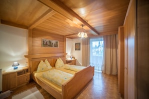 Ein Schlafzimmer mit Holzboden, einem Bett, Nachttischen und einem Fenster mit Vorhängen.