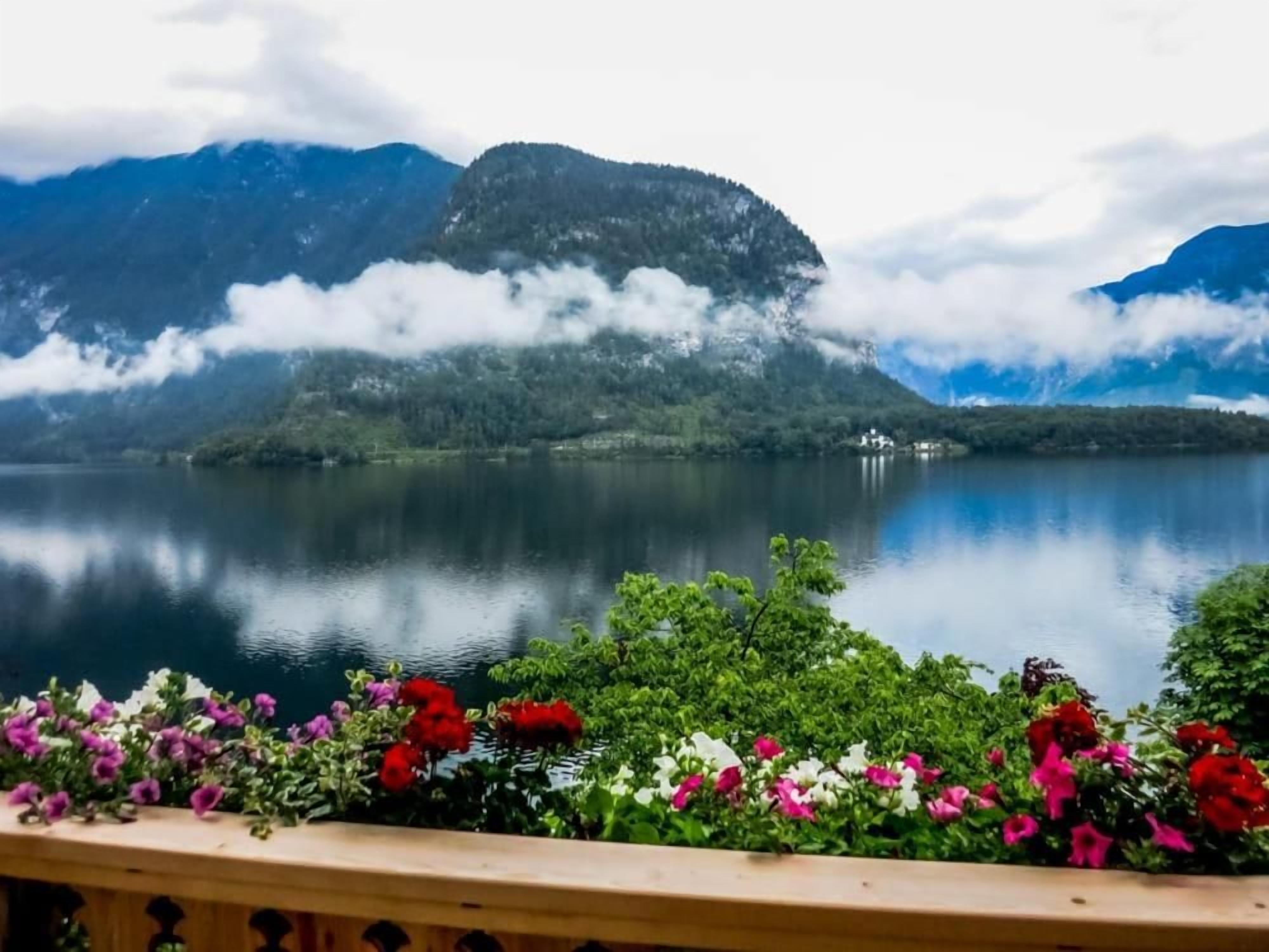 A tranquil lake with mountains in the background and a wooden deck with flowers in the foreground.
