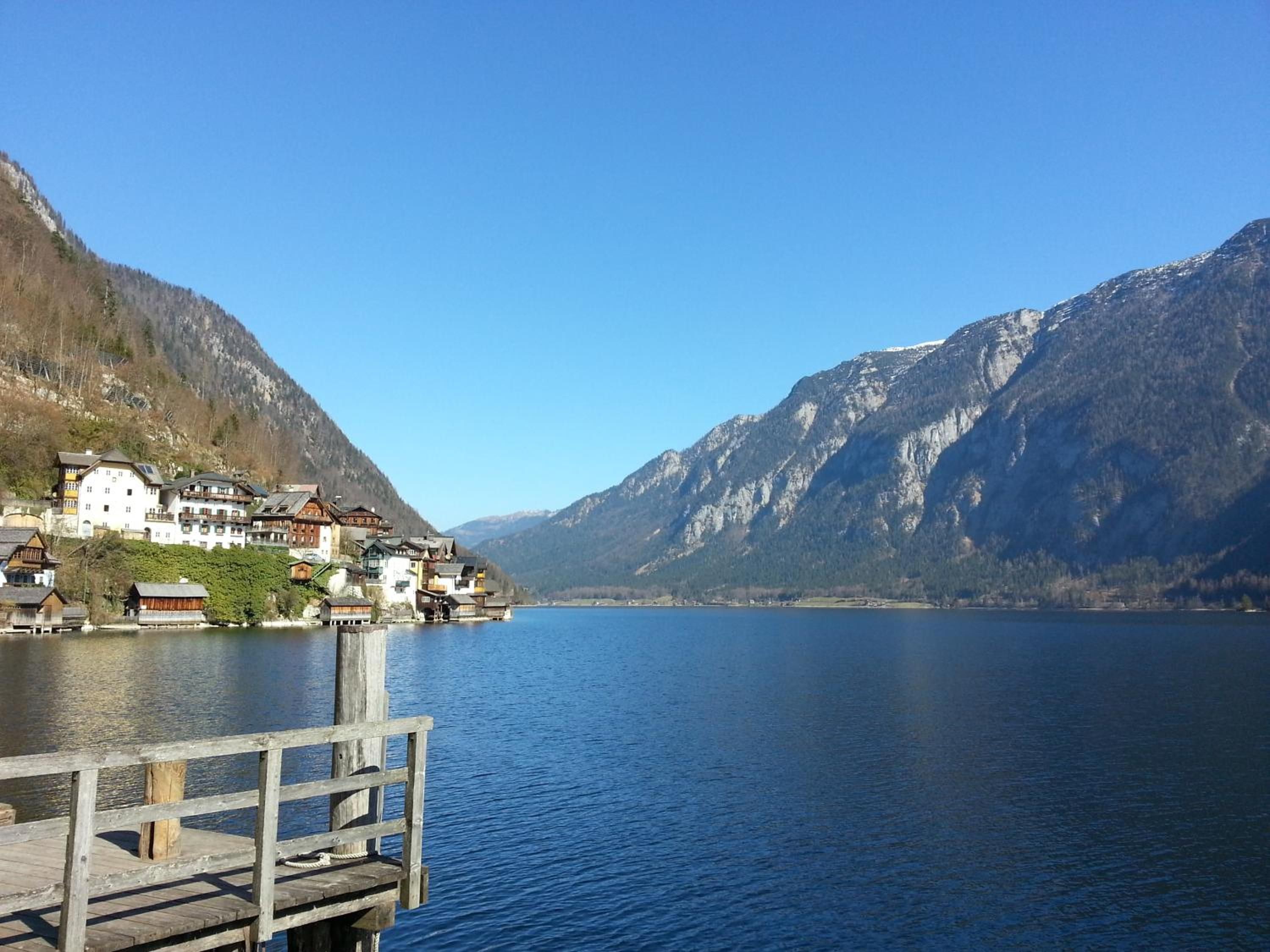 A lakeside village with traditional buildings, a wooden dock, and mountains in the background.