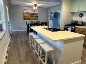 Una cocina moderna con una isla central, taburetes de bar, un comedor con sillas y un cuadro en la pared.