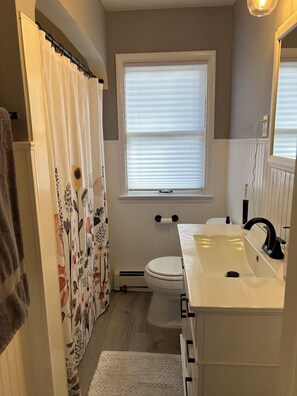 Un baño con inodoro, lavamanos, cortina de ducha y una ventana con persianas.