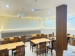 Un restaurante con varias mesas y sillas, un rincón de asientos con banca acolchada, iluminación colgante y una estructura de columna alta.
