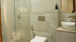 A modern bathroom with a glass-enclosed shower, a toilet, and a sink with a mirror above it. - Hotel Shri Radha Krishnam (Barsana)