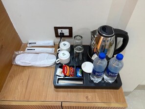 A hotel room with a wooden floor, a small table with a coffee maker, a kettle, a water bottle, and a tray with toiletries. - Hotel Shri Radha Krishnam (Barsana)