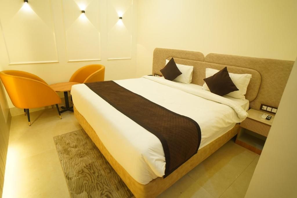 A hotel room with a bed, two pillows, a bedside table, a lamp, and an orange chair.