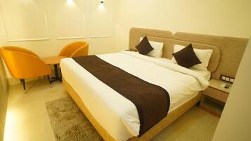 Habitación de hotel con cama, dos almohadas, mesita de noche, lámpara y una silla naranja.