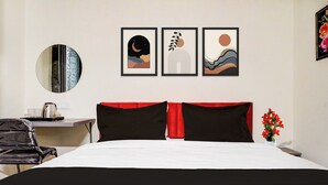 Ett hotellrum med en säng, ett skrivbord och en stol. På väggen hänger tre inramade konstverk.