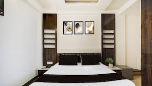 A modern hotel room with a large bed, a bedside table with a phone, a nightstand, and a wall-mounted light fixture. - Super Hotel O GMS Road Formerly The Nest (DEHRADUN)