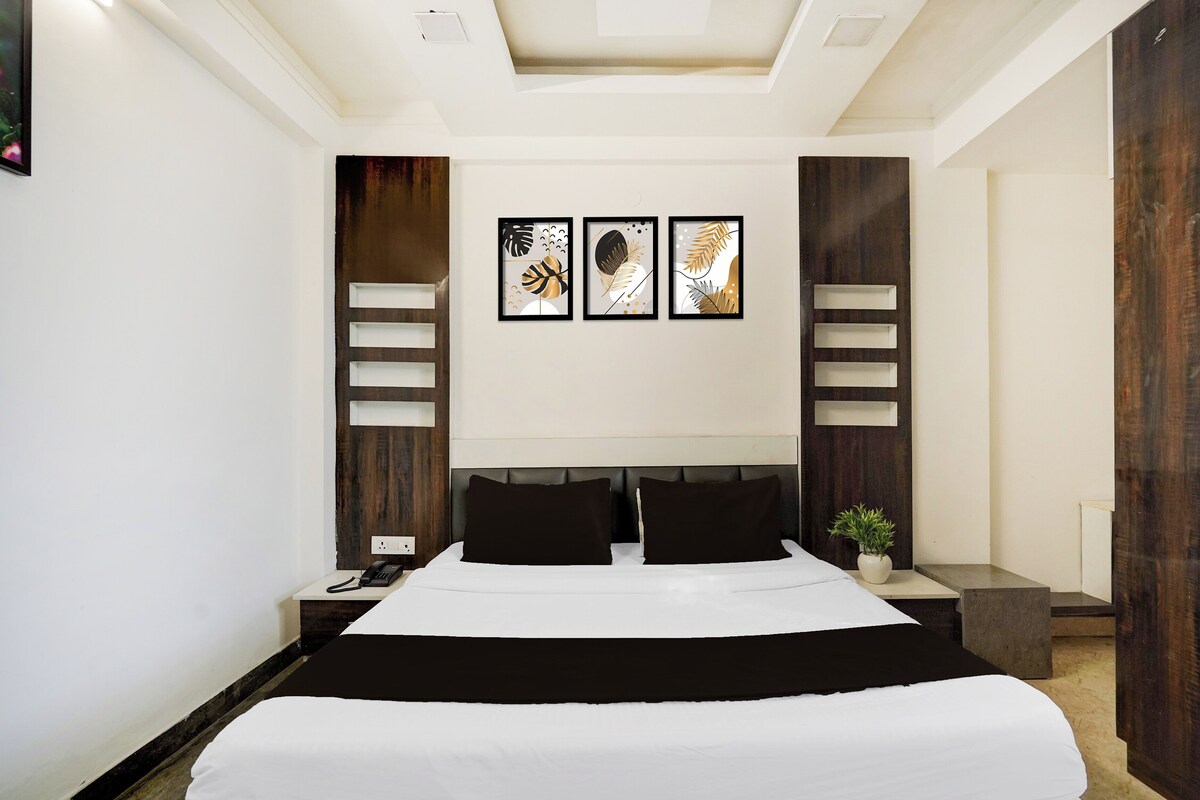 A modern hotel room with a large bed, a bedside table with a phone, a nightstand, and a wall-mounted light fixture.