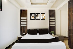 A modern hotel room with a large bed, a bedside table with a phone, a nightstand, and a wall-mounted light fixture. - Super Hotel O GMS Road Formerly The Nest (DEHRADUN)