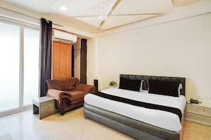 A modern hotel room with a large bed, a brown leather armchair, and a small table. - Super Hotel O GMS Road Formerly The Nest (DEHRADUN)
