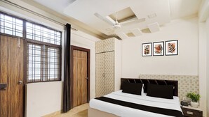 A bedroom with a bed, a ceiling fan, a window with bars, and a door. - Super Hotel O GMS Road Formerly The Nest (DEHRADUN)
