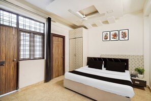 A bedroom with a bed, a ceiling fan, a window with bars, and a door. - Super Hotel O GMS Road Formerly The Nest (DEHRADUN)