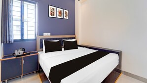 Una habitación de hotel con cama, mesita de noche, ventana con cortinas y una obra de arte en la pared.