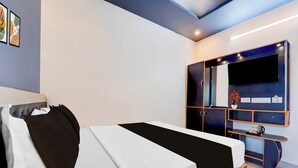 Un dormitorio moderno con cama, armario, televisor y una mesita de noche con un florero.