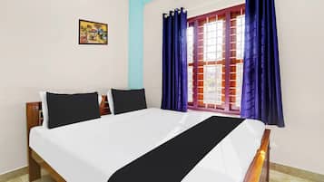 A bedroom with a bed, two pillows, a nightstand, a window with curtains, and a wall-mounted picture.