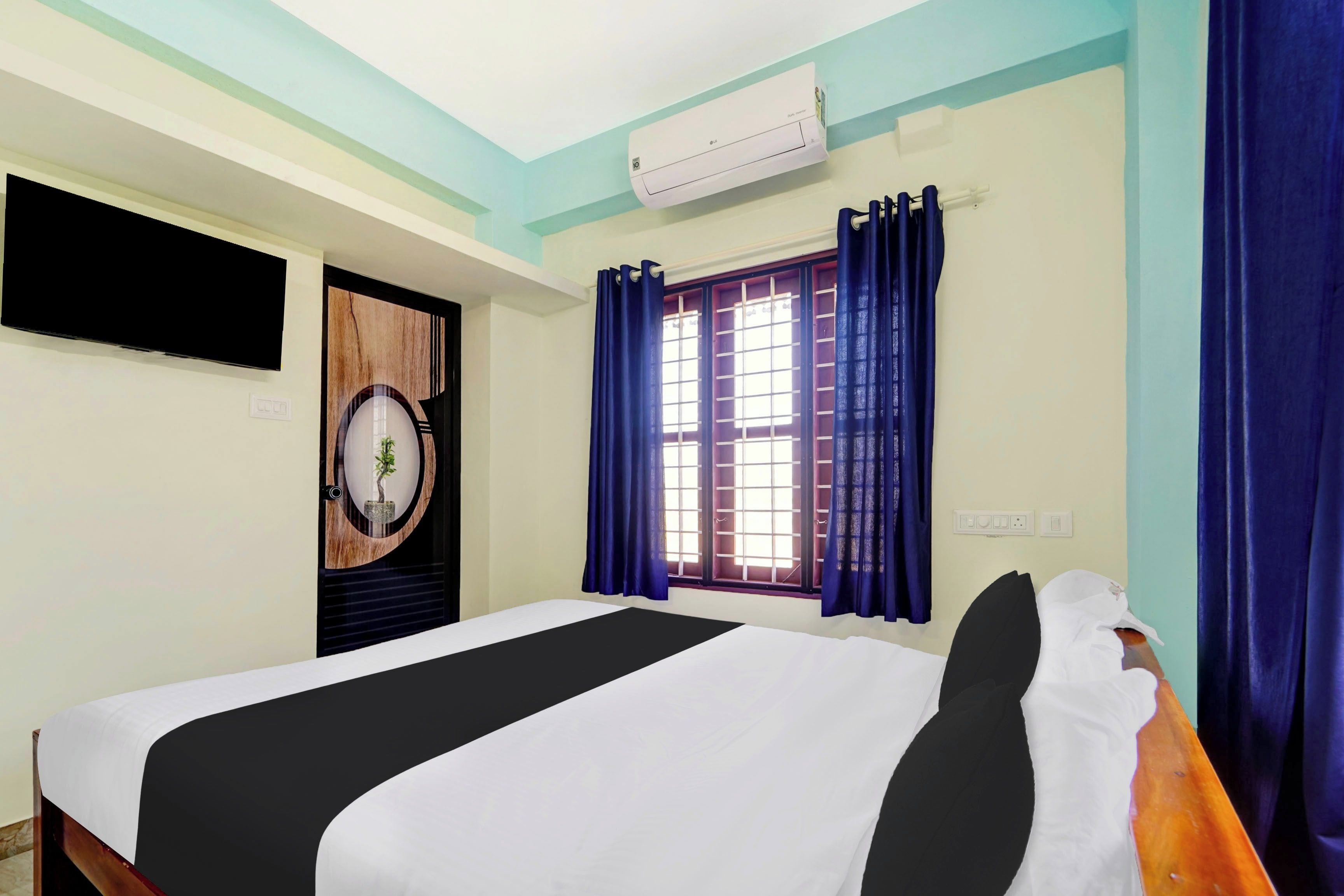 Habitación de hotel con cama, televisor montado en la pared, ventana con cortinas y equipo de aire acondicionado.