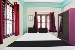 Una habitación con cama, armario y ventana con cortinas.