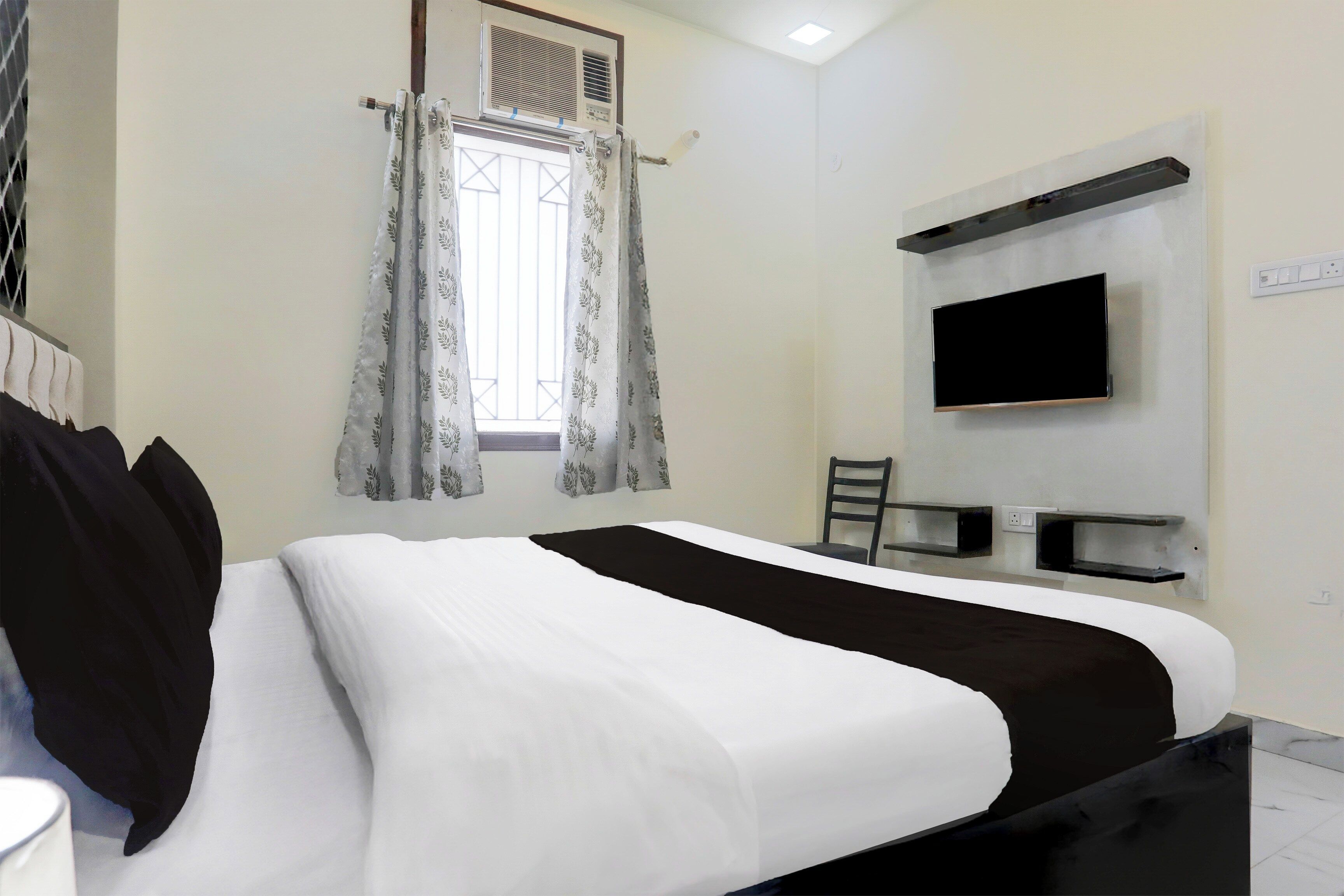 A hotel room with a bed, a flat-screen TV mounted on the wall, and a window with curtains.