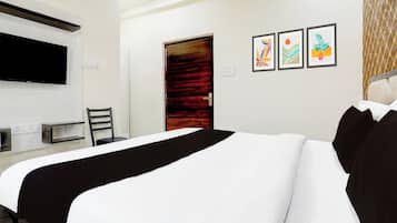 Una habitación de hotel con una cama, un escritorio, una silla, un televisor montado en la pared y tres cuadros enmarcados.