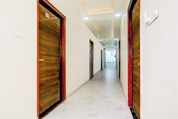 A corridor with doors on both sides, a light switch on the left wall, and a ceiling with recessed lighting.