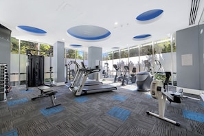 Un gimnasio moderno con máquinas de cardio, equipo de levantamiento de pesas y amplias ventanas.