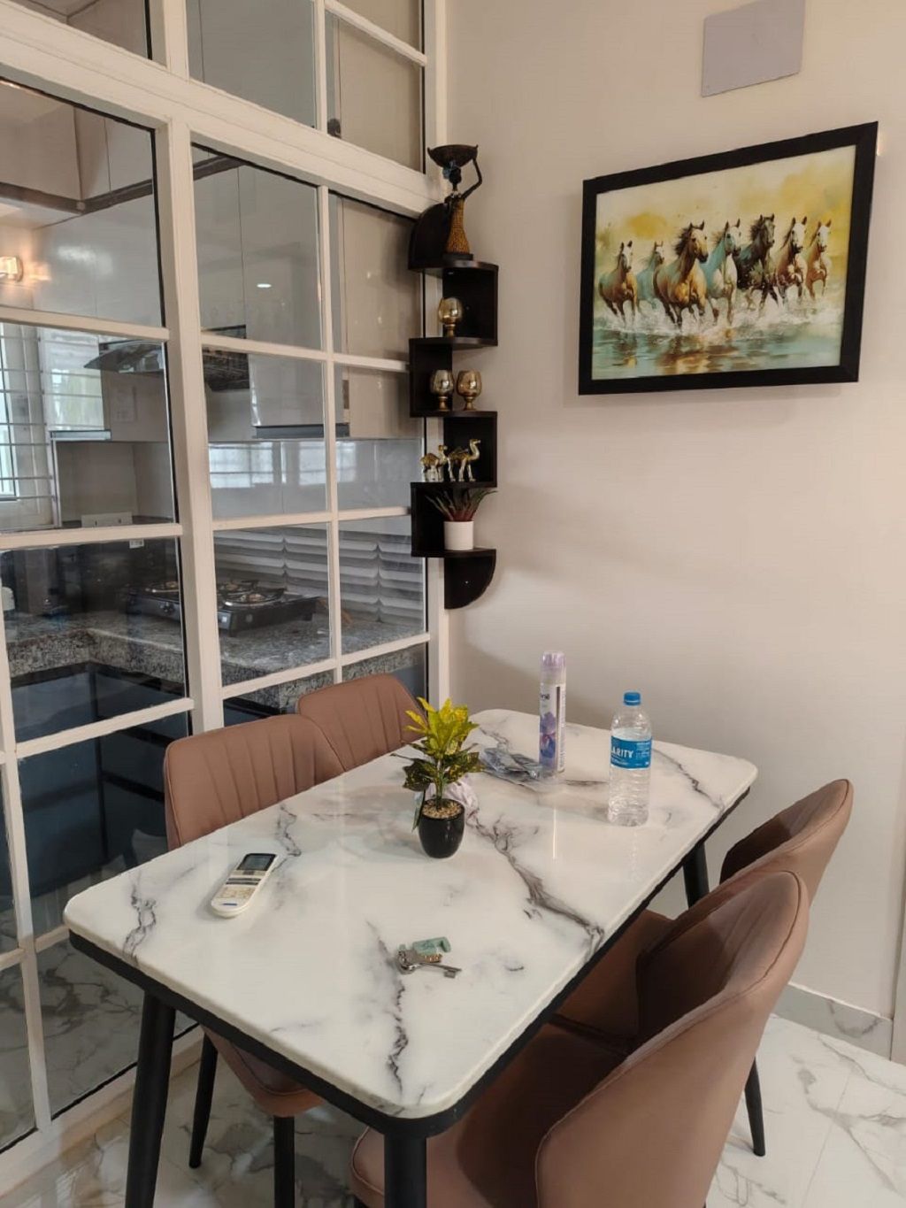 Un coin repas avec une table en marbre, des chaises, une plante en pot, une bouteille d’eau et un tableau encadré accroché au mur.