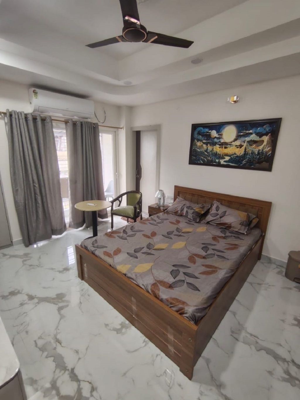 Une chambre à coucher avec un lit, un ventilateur de plafond, un tableau et une fenêtre avec des rideaux.