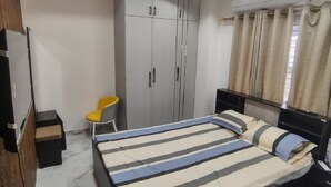 Ein Schlafzimmer mit einem Bett, einem Kleiderschrank, einem Deckenventilator und einer kleinen Sitzecke.
