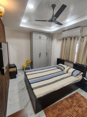 Ein Schlafzimmer mit einem Bett, einem Kleiderschrank, einem Deckenventilator und einer kleinen Sitzecke.
