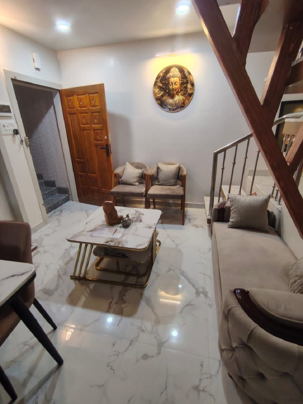 Uma sala de estar com piso de mármore, uma mesa de centro, duas poltronas, um sofá e uma escada de madeira.